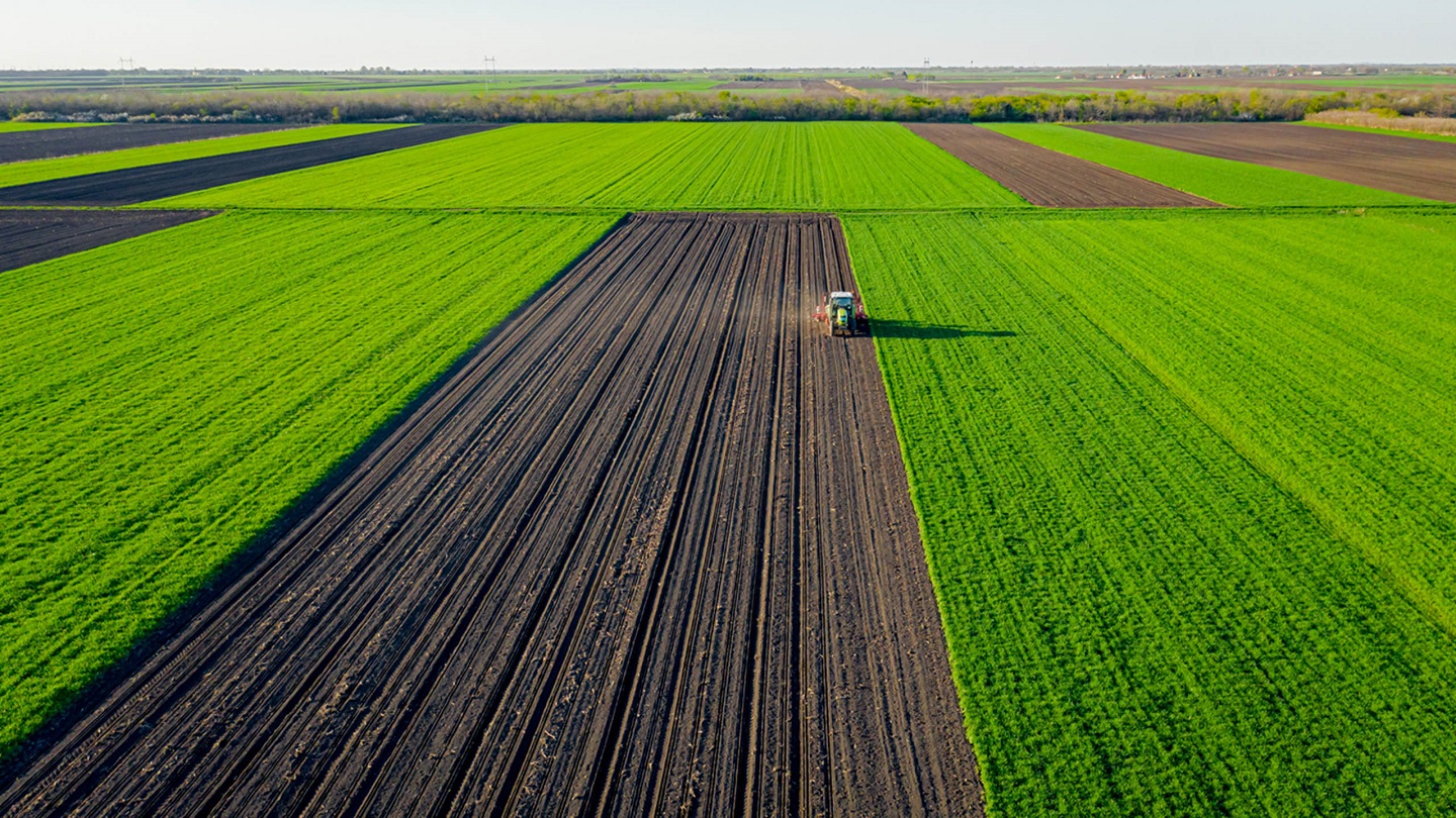 Above view, of tractor as pulling mechanical seeder machine over arable field, soil, planting new cereal crop, corn, maize.